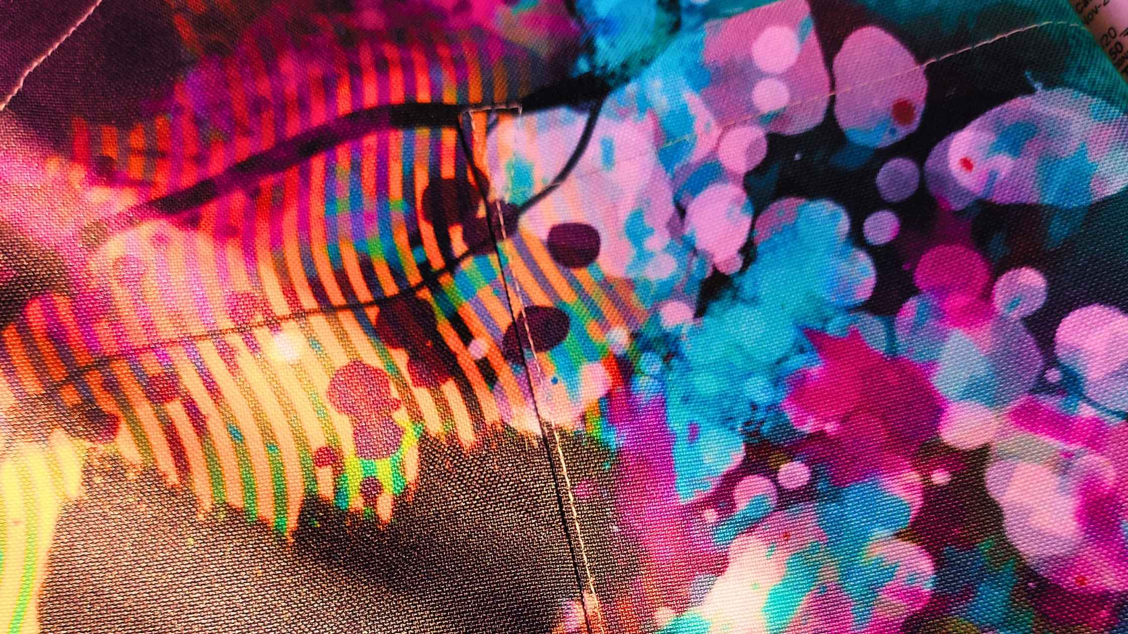 Closeup of the Neuro-Spicy Brain original design apron by Kylyne’s Custom Treasures, showing vibrant turquoise, magenta, and gold abstract patterns with detailed stitching and fabric texture.