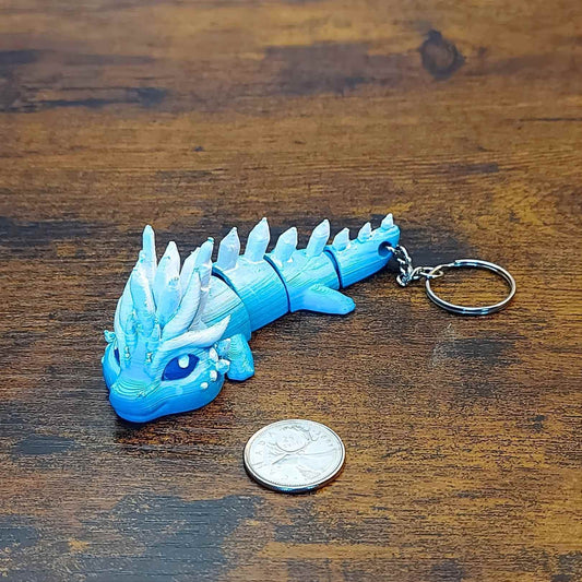 Keychain size Eryndra the Ice Elemental Dragon of Drakora, 3D-printed and hand-painted by Kylyne’s Custom Treasures, displayed on a wood background with a coin for scale.