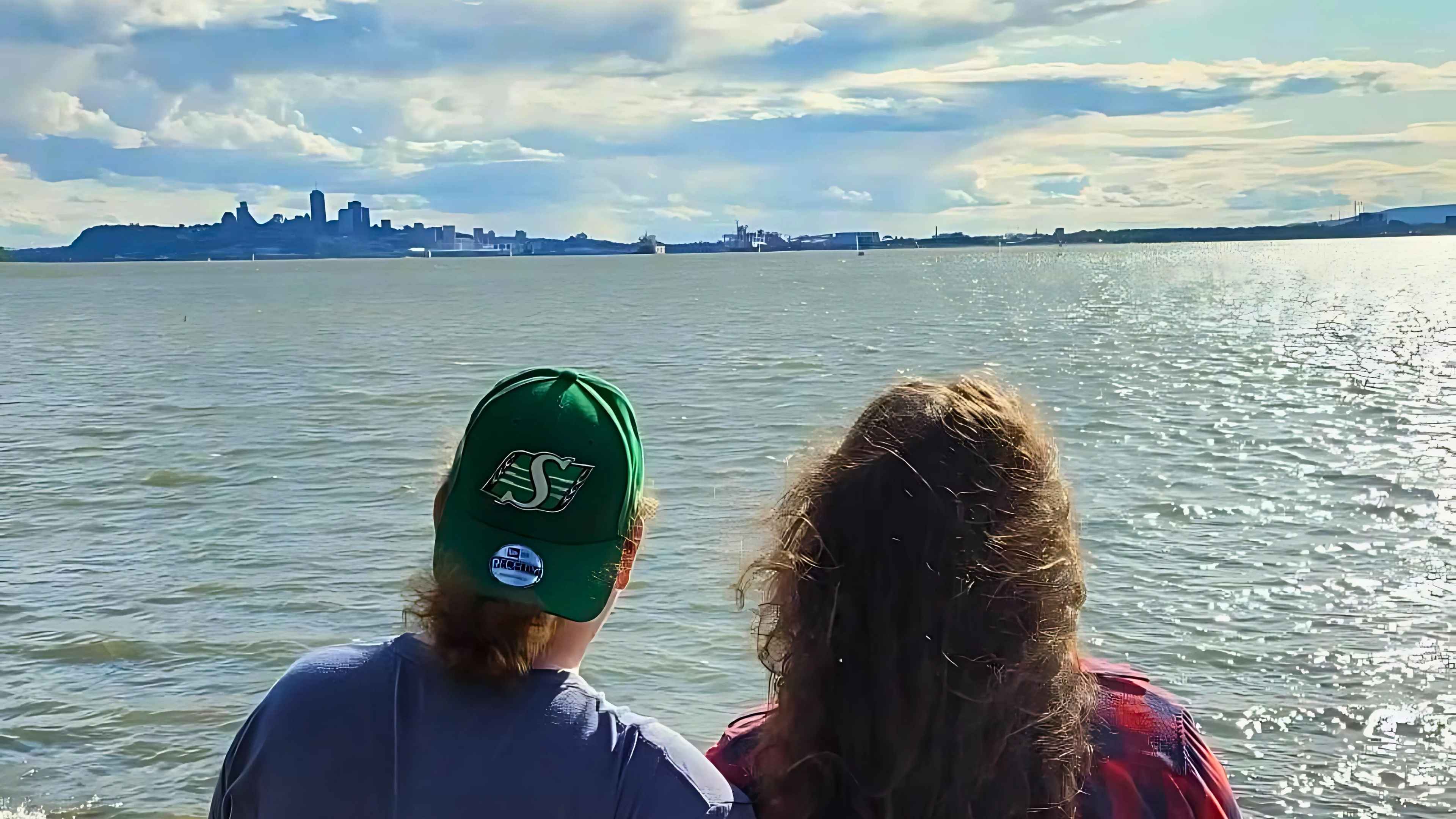 Carolyne and Kyle sitting together, looking out over the water toward the skyline of Quebec City from the tip of Ăle d'OrlĂ©ans (Sainte-PĂ©tronile), sharing a peaceful moment at their favorite spot.