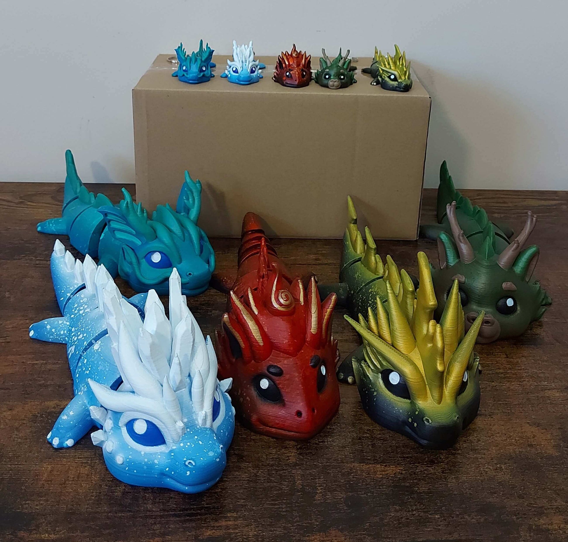 Five hand-painted elemental dragons - sea, ice, fire, forest, and thunder - articulated fidget companions crafted for neurodivergent minds by Kylyne's Custom Treasures