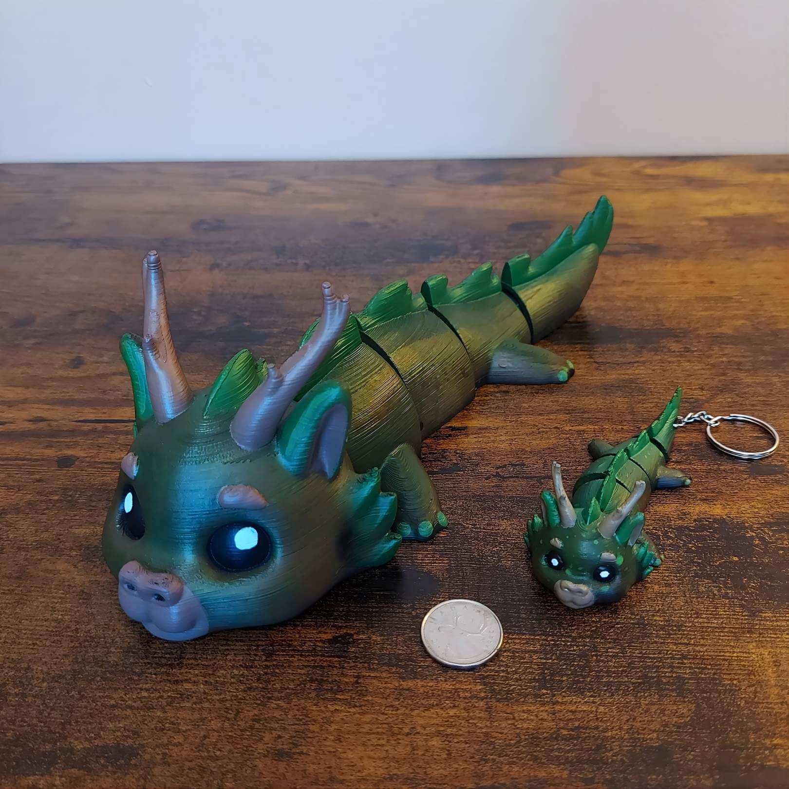 Large and keychain size Dasyra the Forest Elemental Dragon of Drakora, 3D-printed and hand-painted by Kylyne’s Custom Treasures, displayed on a wood background with a coin for scale.