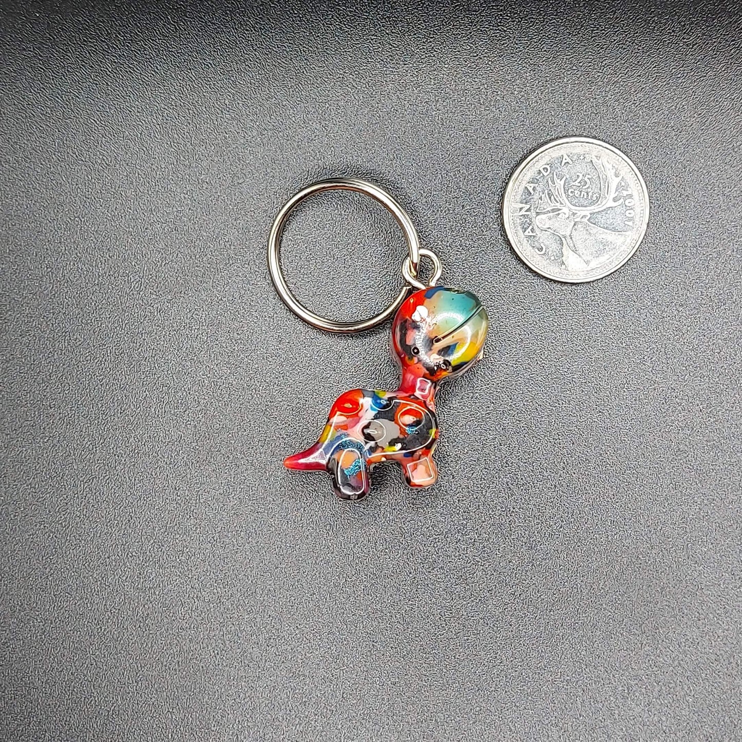 Upcycled 3D-printed dopamine dangle keychain in the shape of a colorful dinosaur, created by Kylyne’s Custom Treasures, displayed on a beige background.