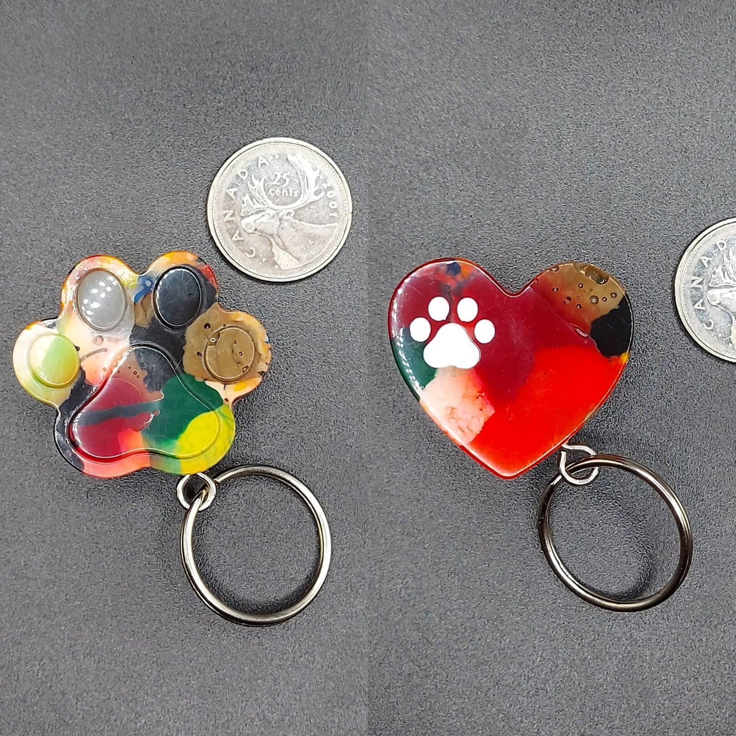 Upcycled 3D-printed dopamine dangle keychains by Kylyne’s Custom Treasures, featuring a multicolor paw print and a red heart with white paw print, displayed with Canadian quarters for size reference.