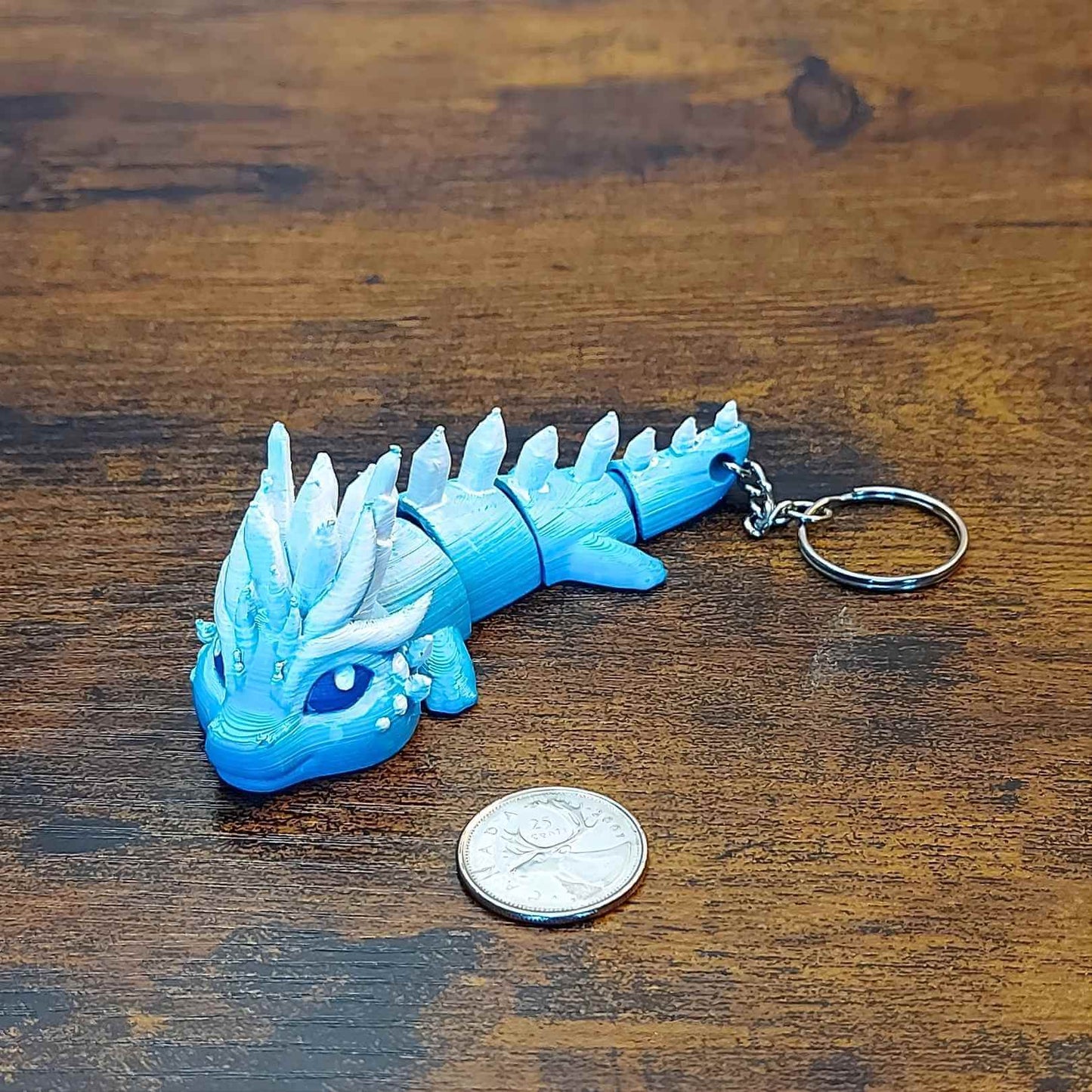 Keychain size Eryndra the Ice Elemental Dragon of Drakora, 3D-printed and hand-painted by Kylyne’s Custom Treasures, displayed on a wood background with a coin for scale.