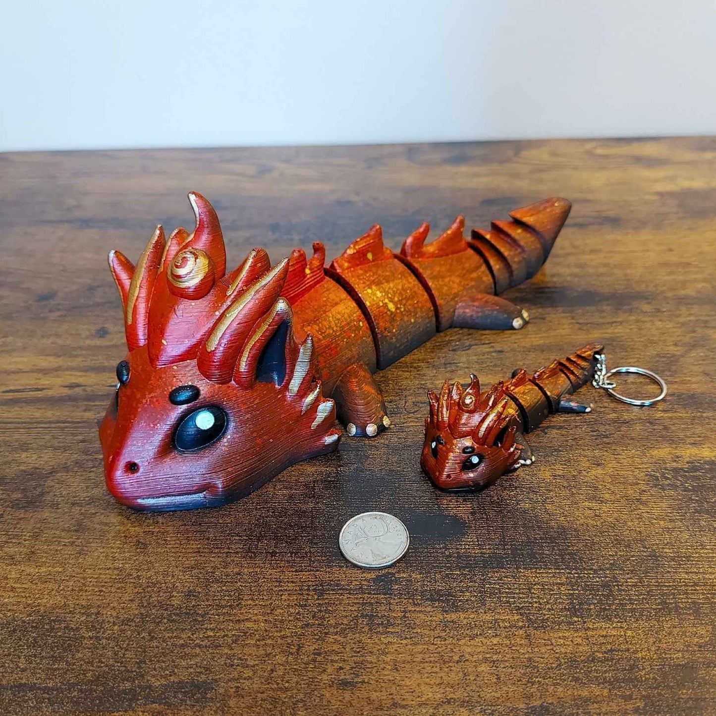 Large and keychain size Kaelix the Fire Elemental Dragon of Drakora, 3D-printed and hand-painted by Kylyne’s Custom Treasures, displayed on a wood background with a coin for scale.

