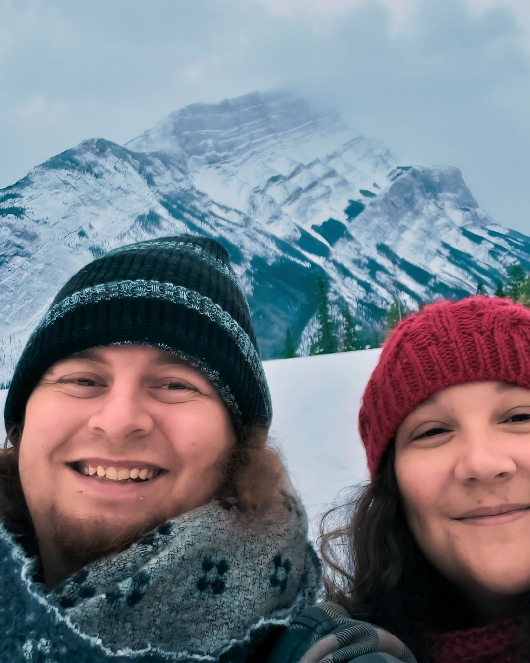 Kyle and Carolyne bundled up together in Banff with mountain views in the background, capturing a joyful part of their Canadian love story.