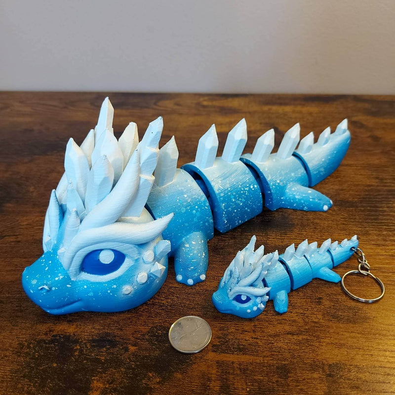 Large and keychain size Eryndra the Ice Elemental Dragon of Drakora, 3D-printed and hand-painted by Kylyne’s Custom Treasures, displayed on a wood background with a coin for scale.