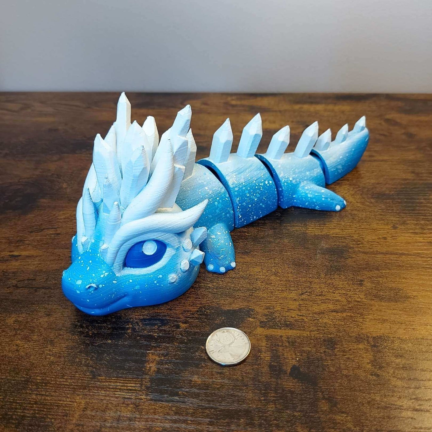 Large Eryndra the Ice Elemental Dragon of Drakora, 3D-printed and hand-painted by Kylyne’s Custom Treasures, displayed on a wood background with a coin for scale.