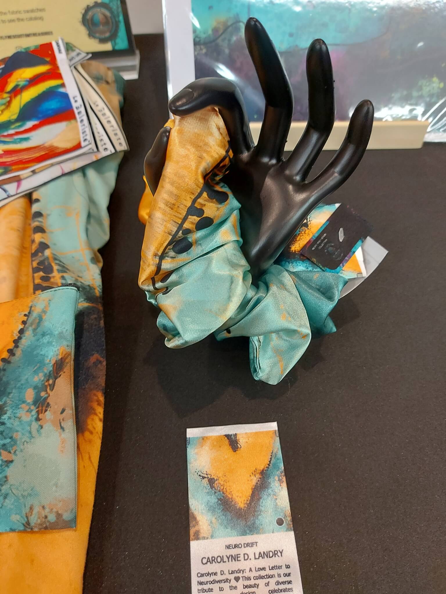 Neuro Drift satin jumbo scrunchie in teal and orange print displayed on a market table