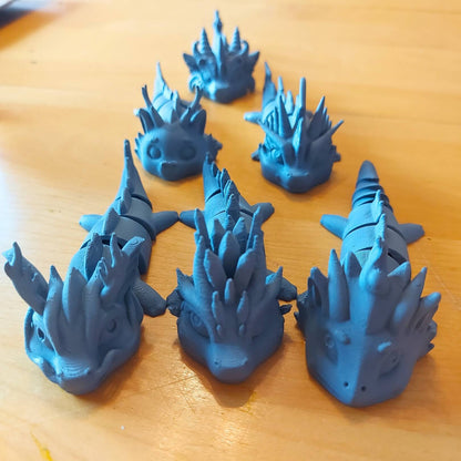 Six primed dragon keychain examples for the Paint Your Dragon Kit arranged on a wooden surface.