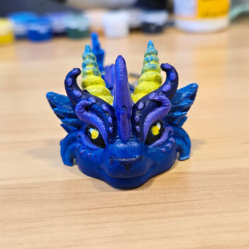 Front view of a customer-painted finished example from the Paint Your Dragon Kit: dark blue dragon with yellow stars and bright eyes on a wooden surface.