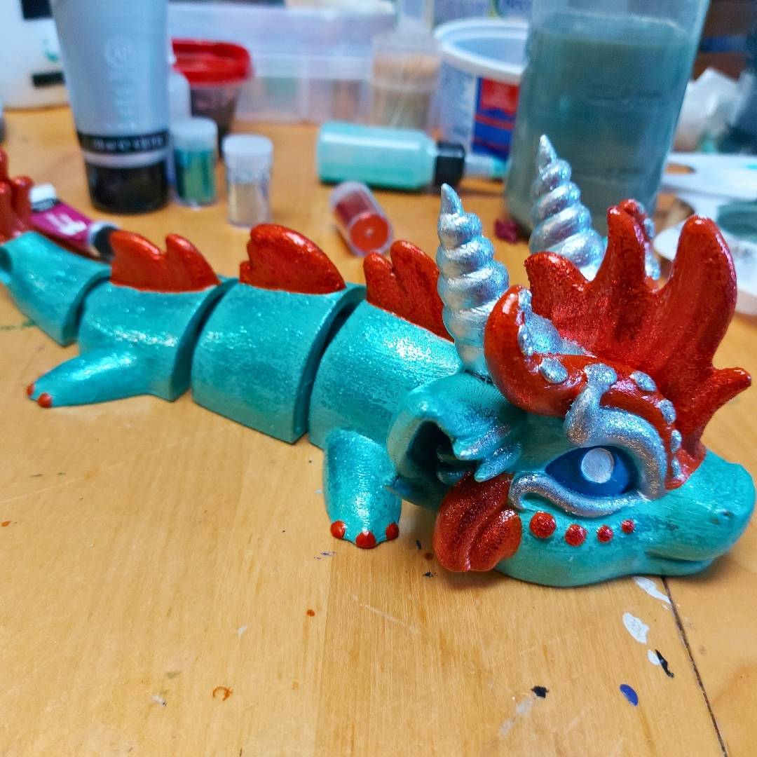 Finished example of a hand-painted showgirl dragon from the Paint Your Dragon Kit, teal with red details, photographed on a work table.