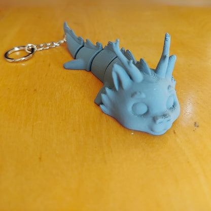 Primed Dasyra dragon keychain from the Paint Your Dragon Kit before painting, shown on a wooden surface.