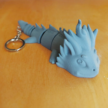 Primed Kaelix dragon keychain from the Paint Your Dragon Kit before painting, shown on a wooden surface.