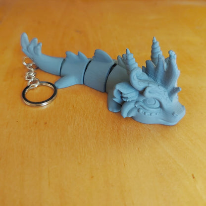 Primed Zephir dragon keychain from the Paint Your Dragon Kit before painting, shown on a wooden surface.