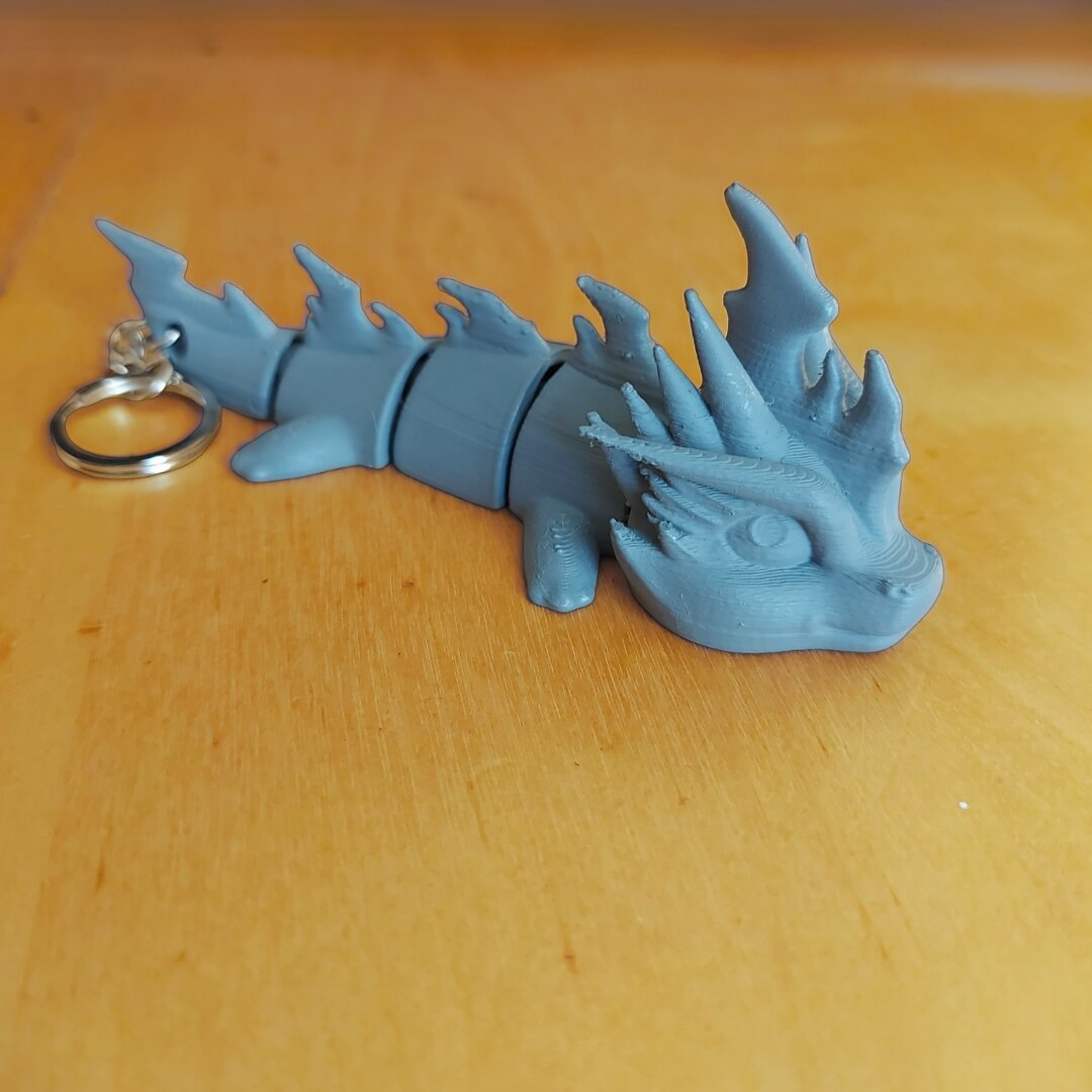 Primed Zoryn dragon keychain from the Paint Your Dragon Kit before painting, shown on a wooden surface.