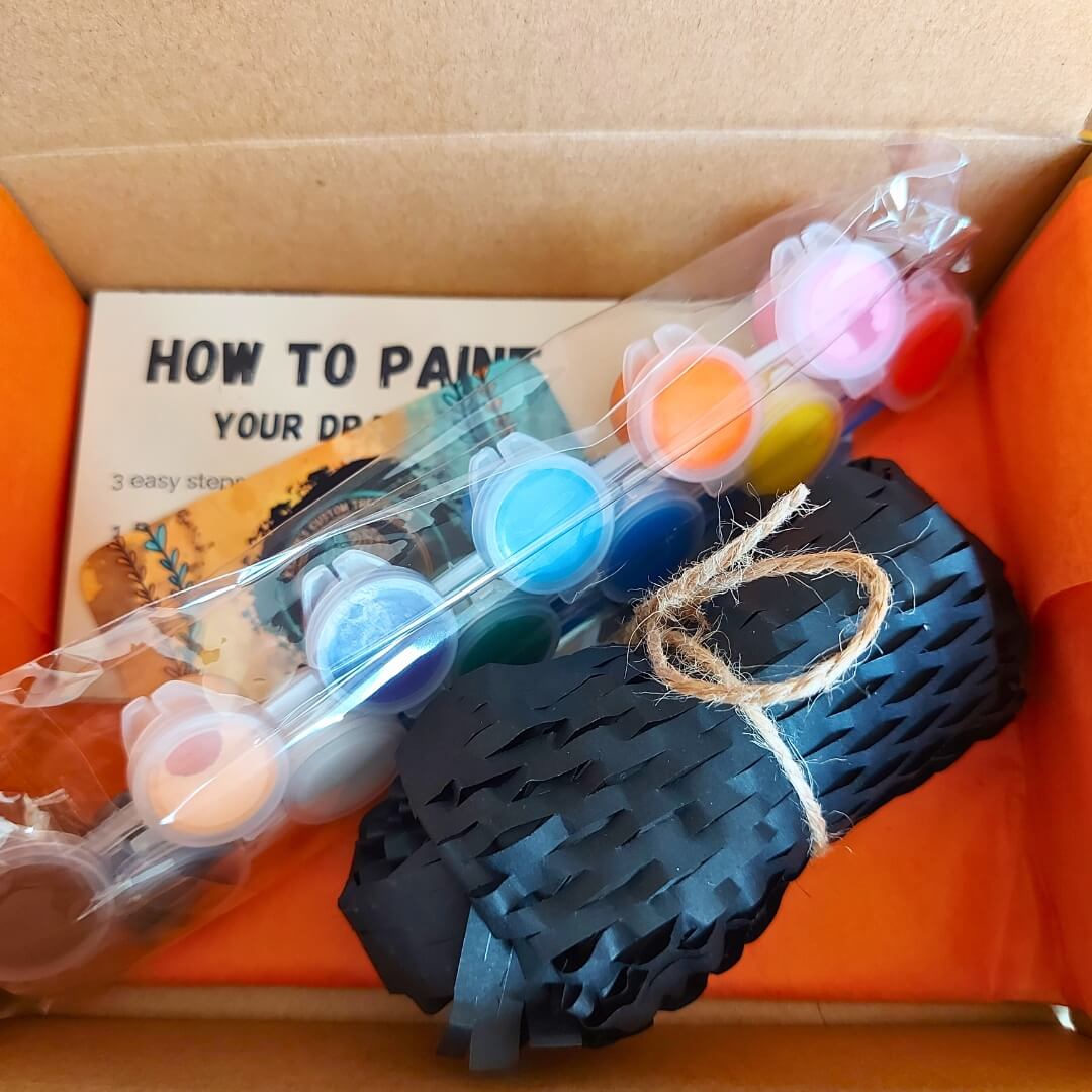 Inside the Paint Your Dragon Kit box showing acrylic paint pods, instruction card, and protective packing paper.