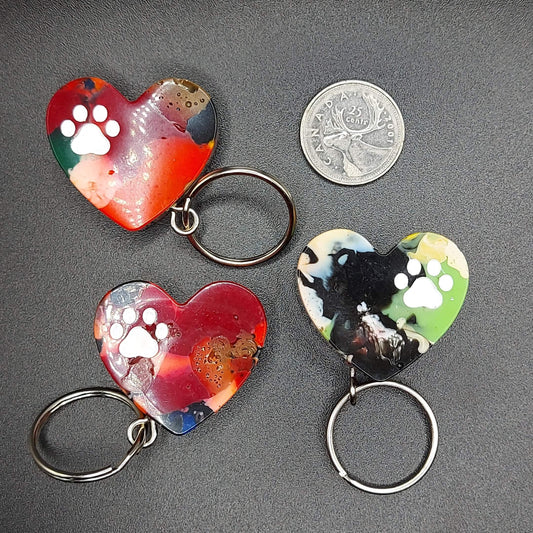Set of three dopamine dangles upcycled 3D-printed heart-shaped keychains with white paw prints, created by Kylyne’s Custom Treasures, displayed with a Canadian quarter for size reference.