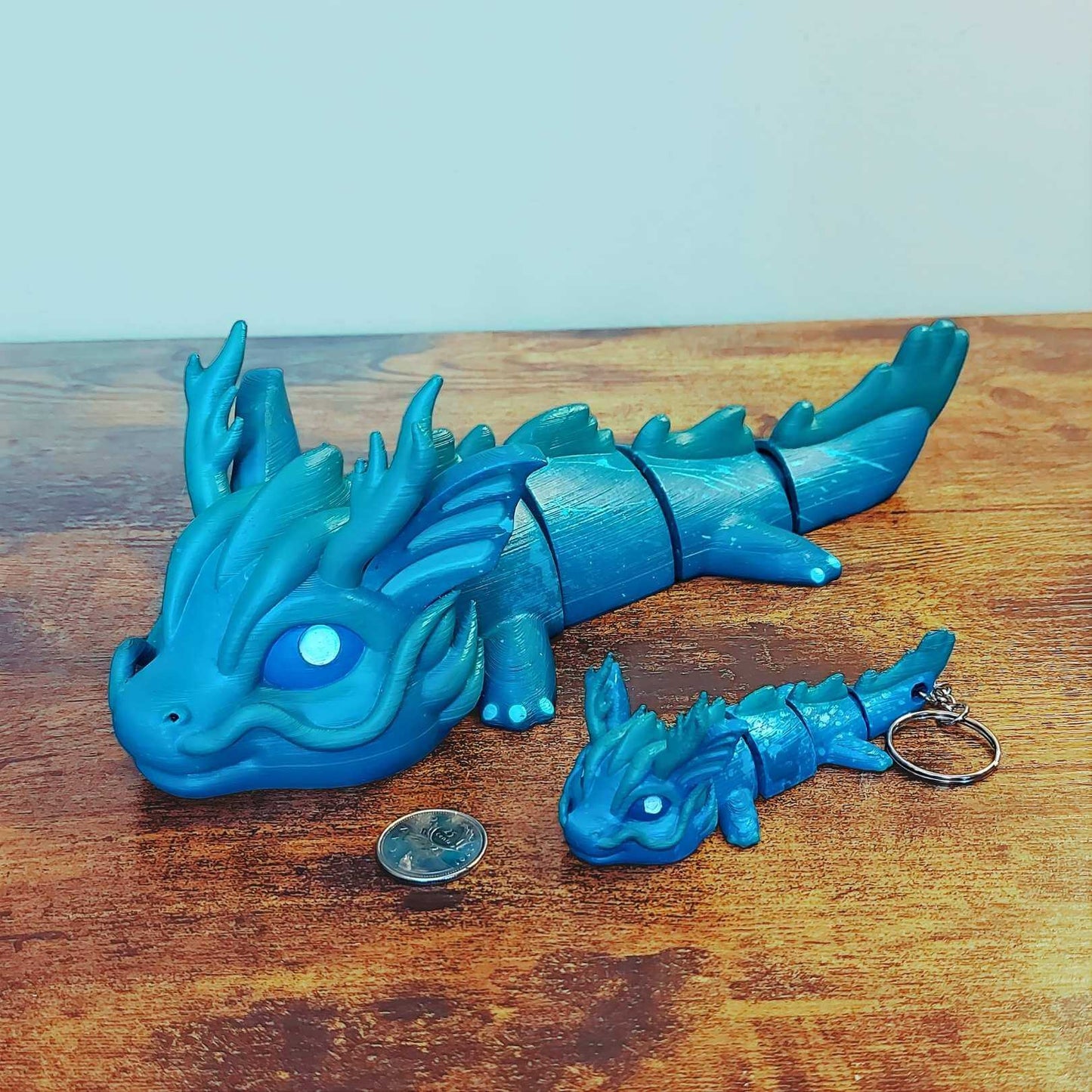 Large and keychain size Vaylen the Sea Elemental Dragon of Drakora, 3D-printed and hand-painted by Kylyne’s Custom Treasures, displayed on a wood background with a coin for scale.